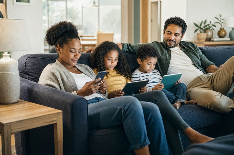 Family of four on a sofa, each using a phone or tablet